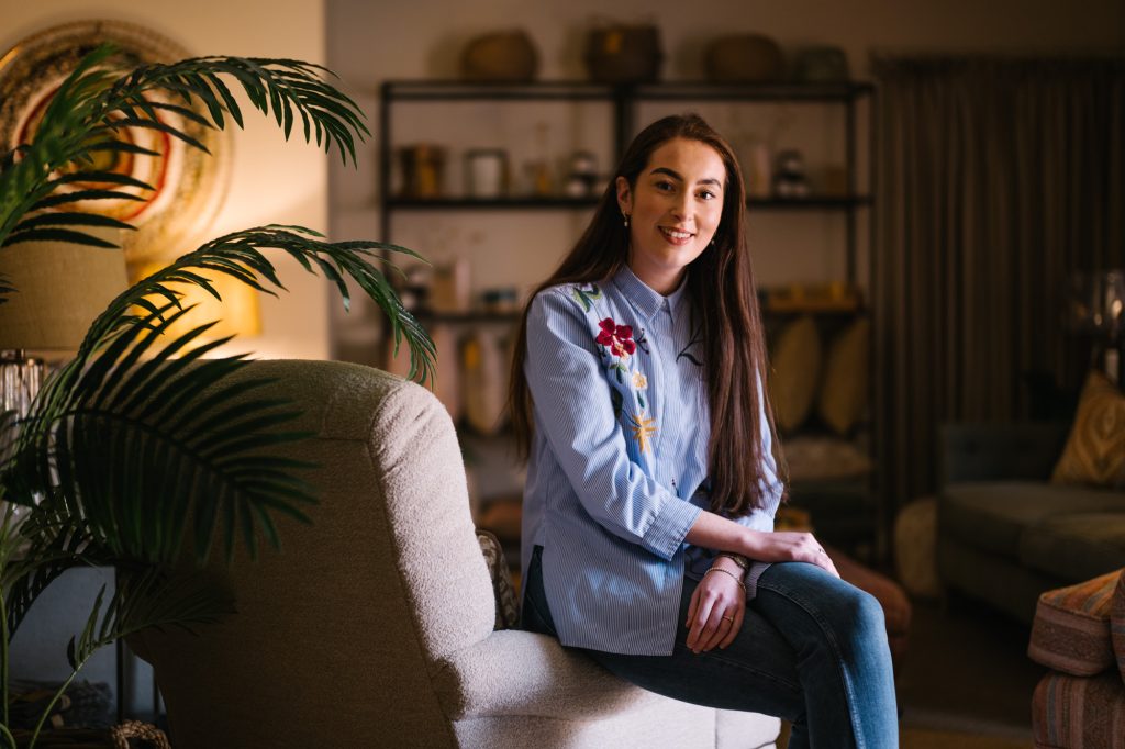 Smiling woman sitting indoors on an armchair in a warmly lit room.