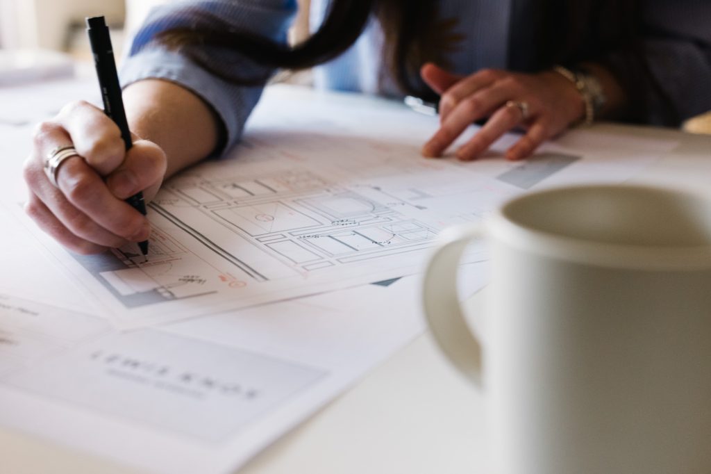 Woman sketching on architectural floor plans at a desk, with a mug of tea in the foreground