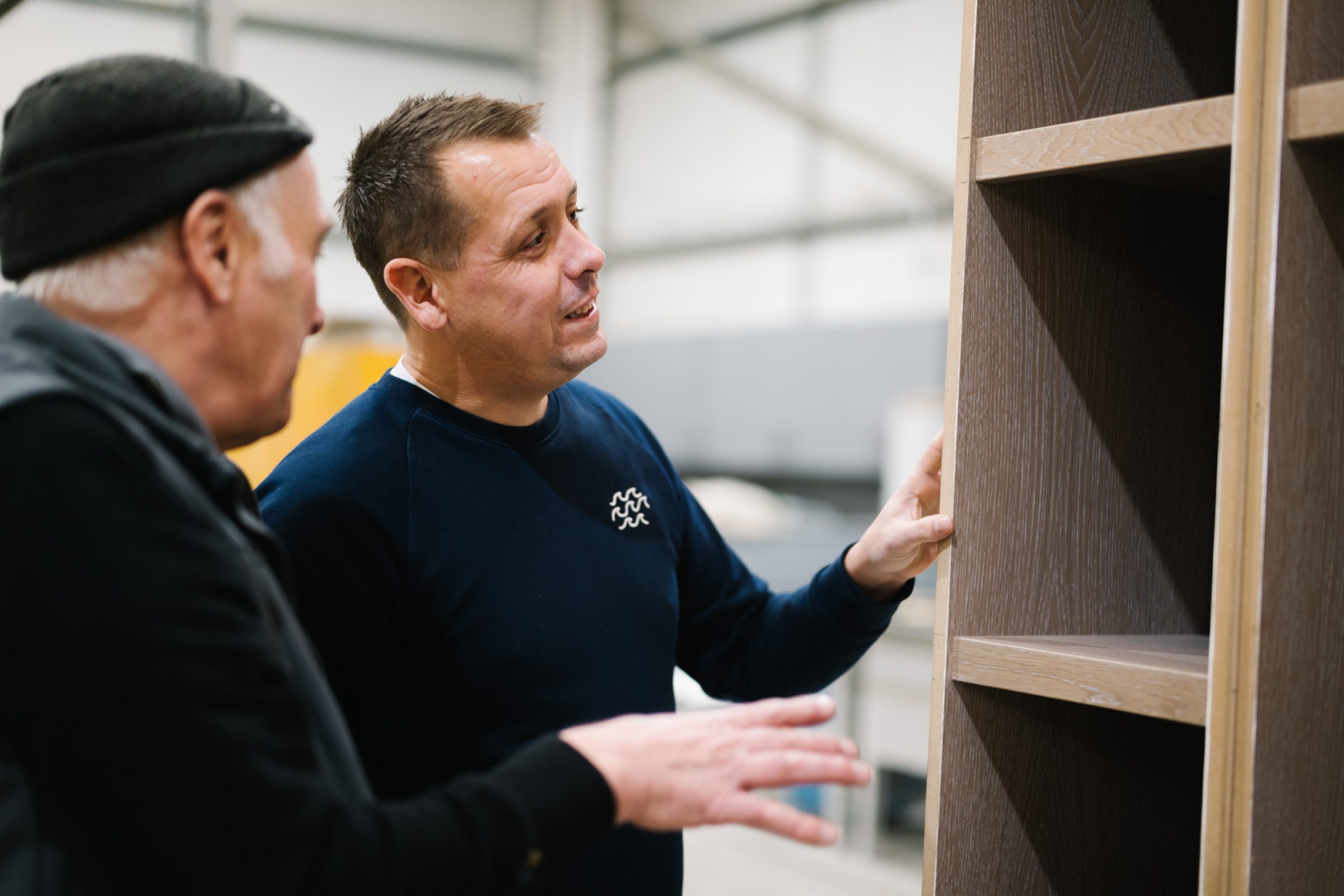 Simon & Client looking at a wooden shelving unit in a workshop.