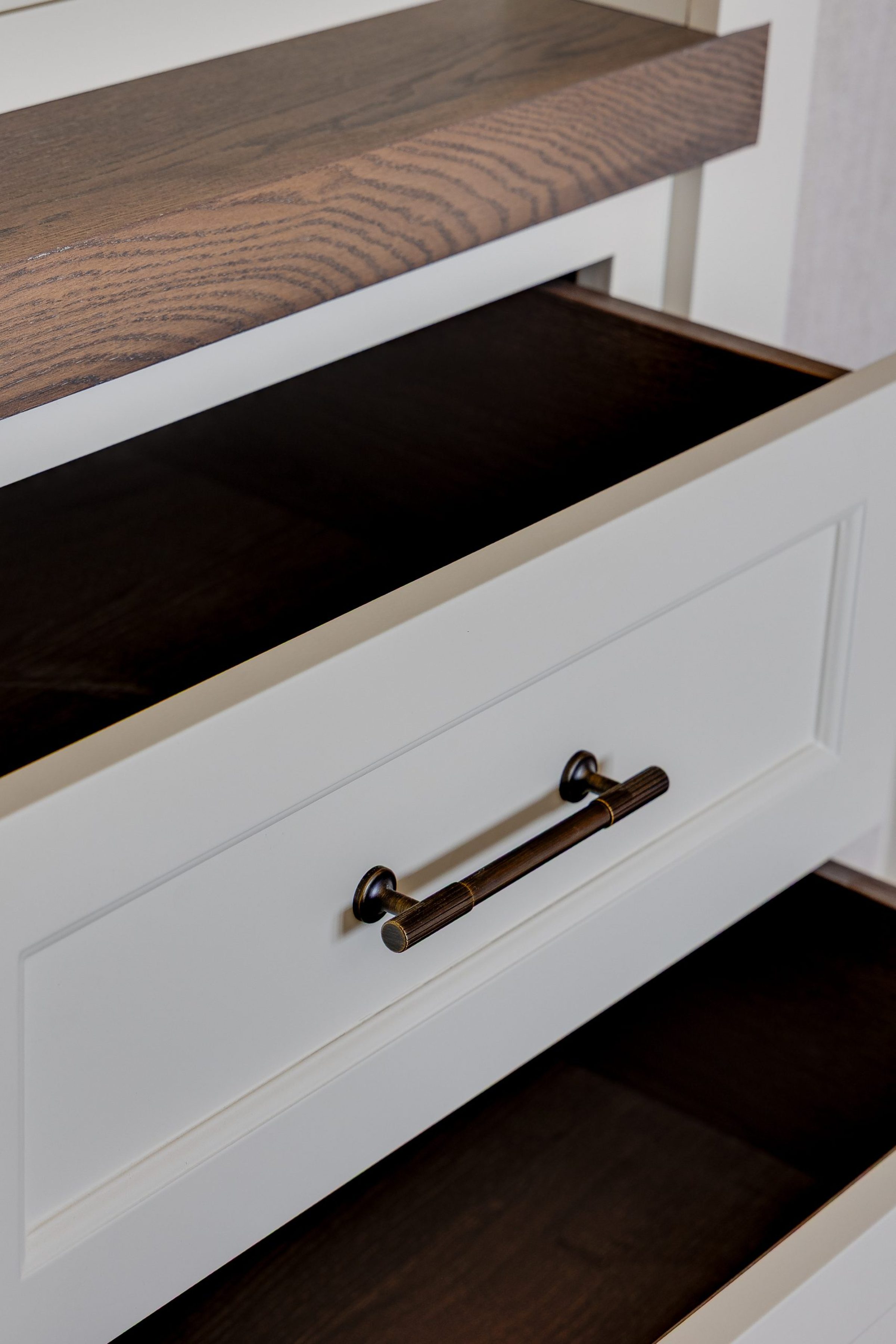 Close-up of an open drawer with a dark wood interior and brass handle.