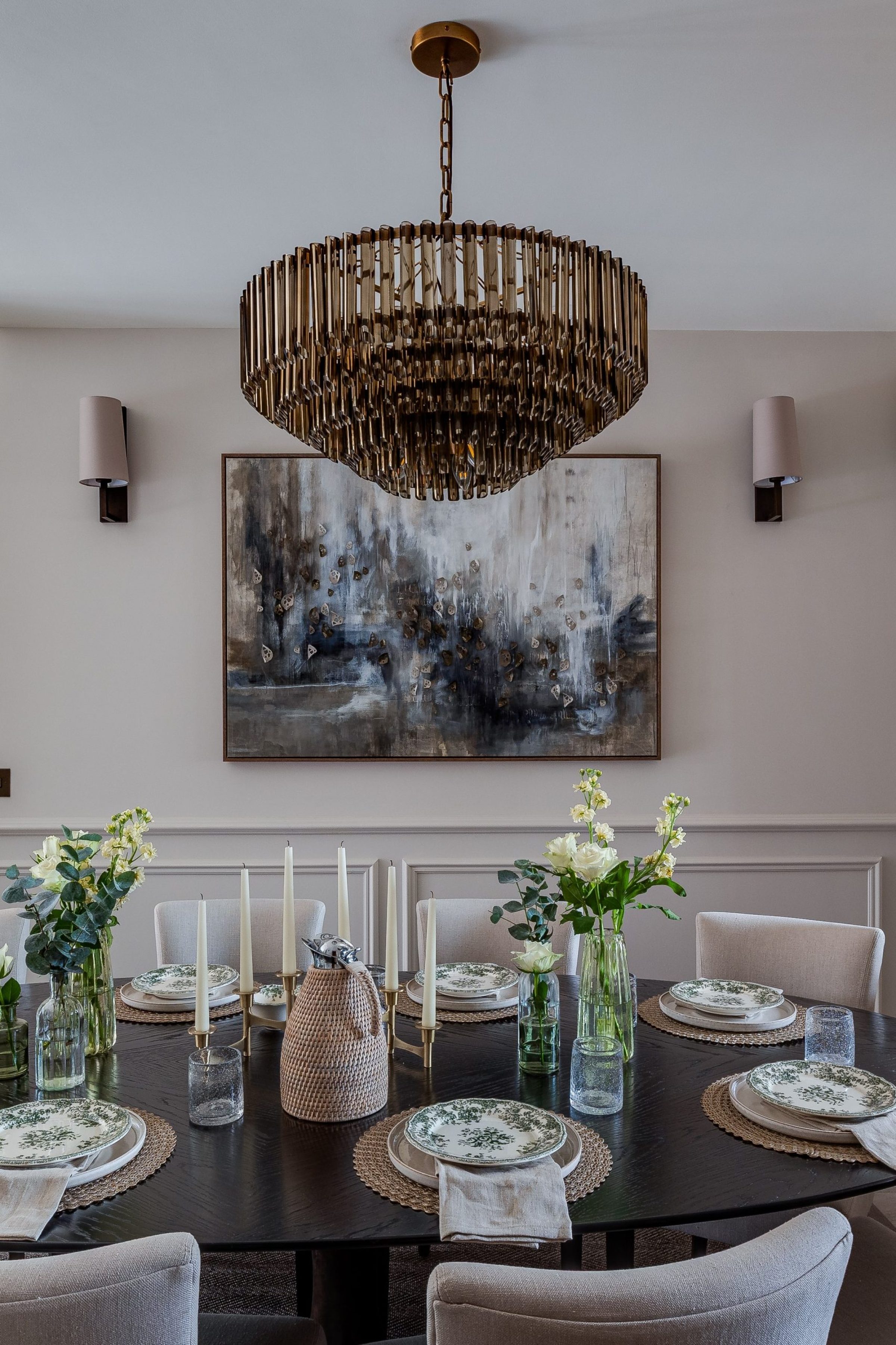 Layered dining table setting with soft linen, candles and natural accents beneath a statement pendant.