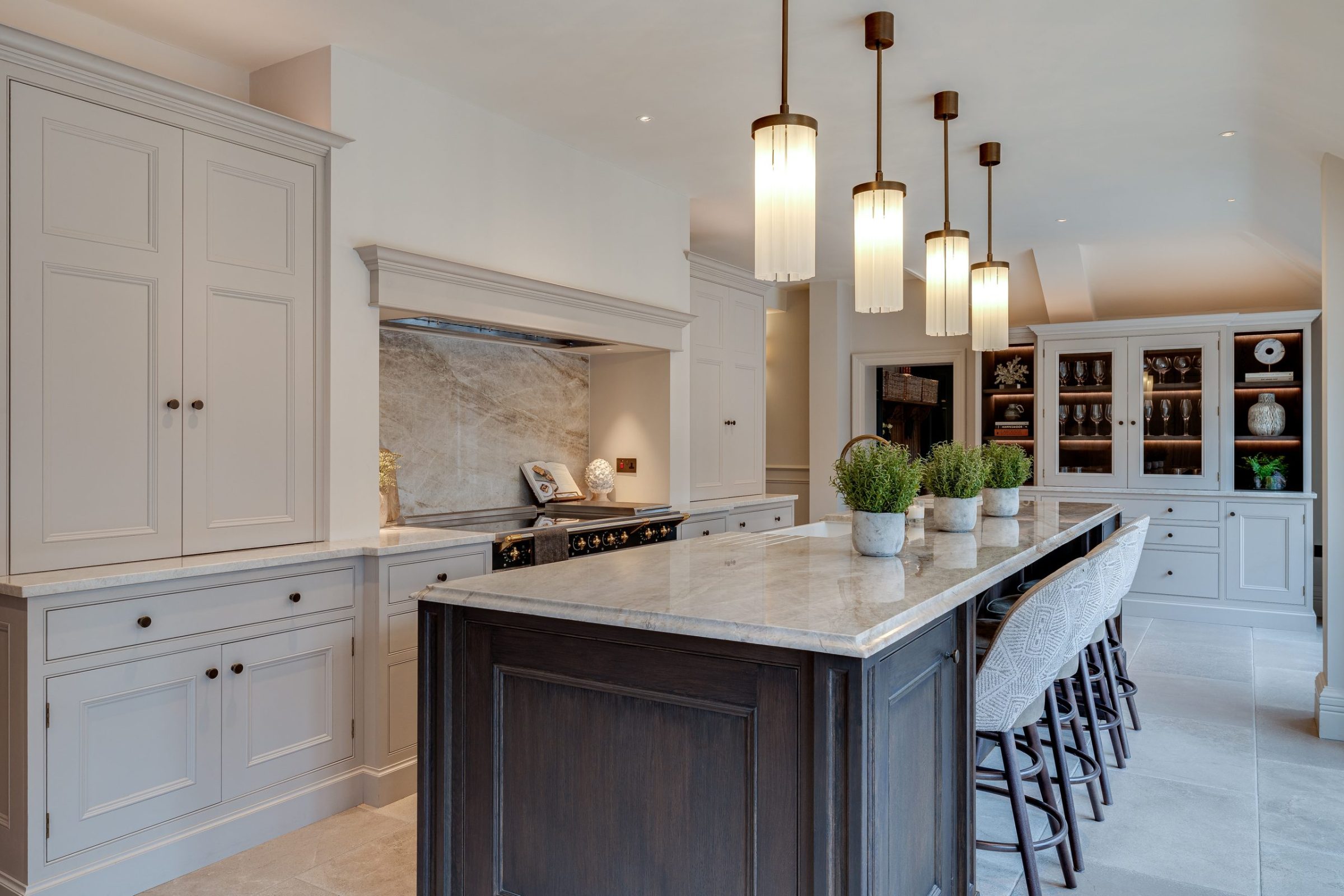 Large kitchen island with stone worktop, dark base units and pendant lights