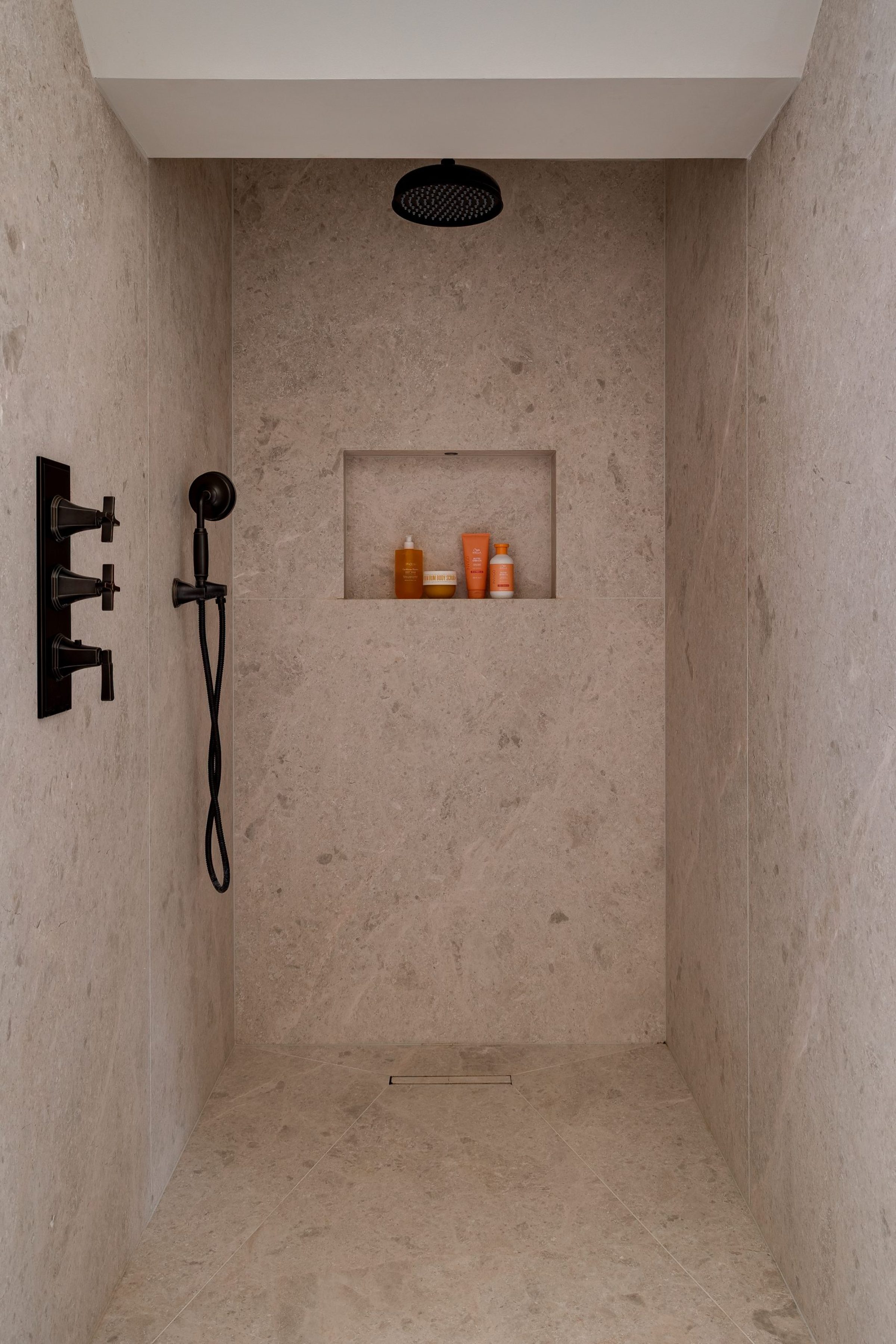 Walk-in shower with limestone walls, matte black fixtures and recessed niche