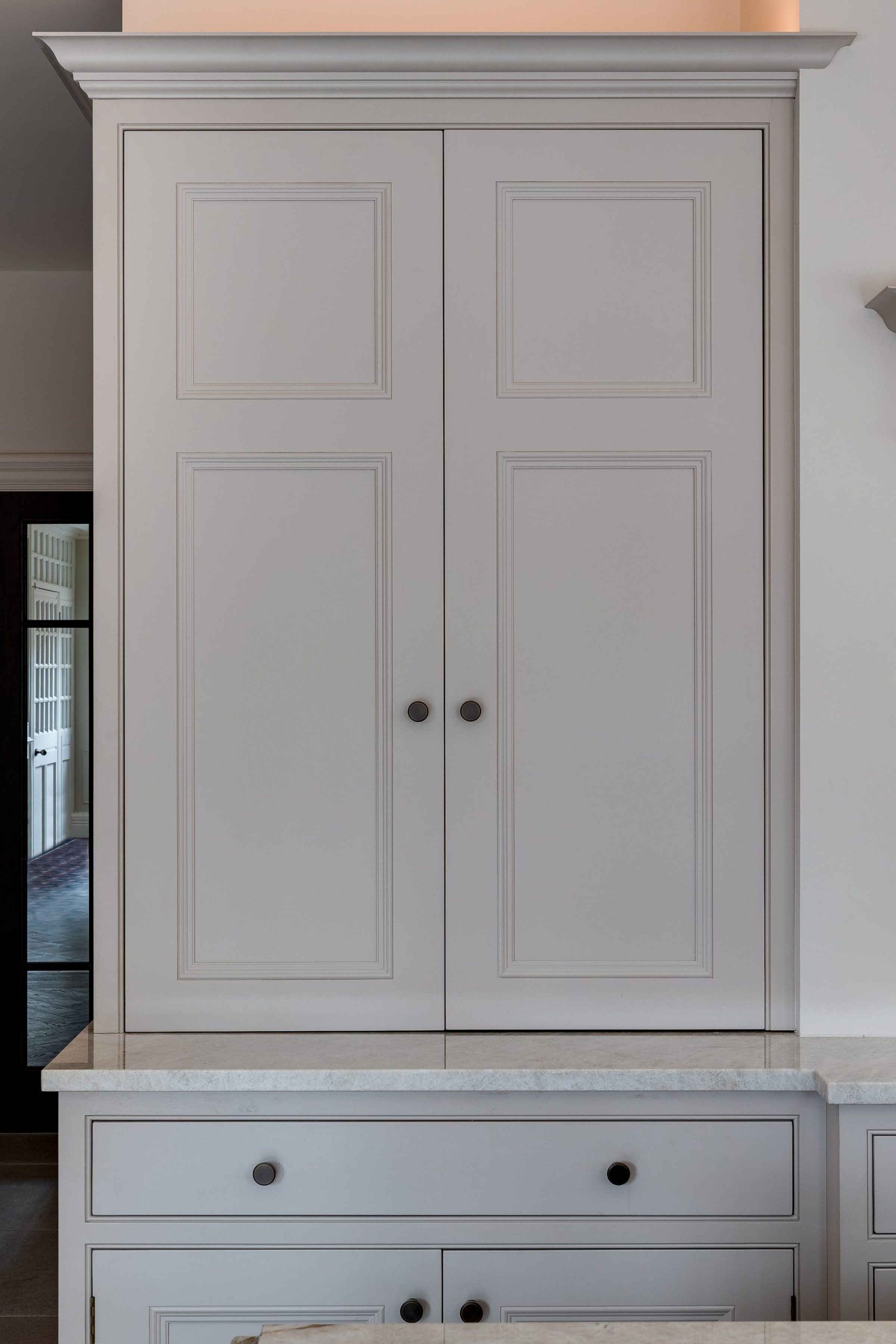 Closed built-in kitchen larder with painted panelled doors and marble countertop.