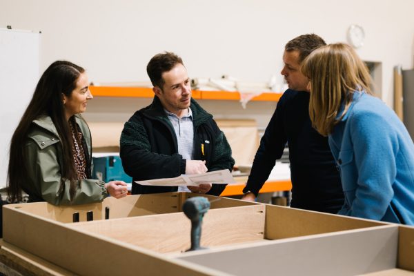 Lewis Knox team members discussing plans around a wooden frame in a workshop.