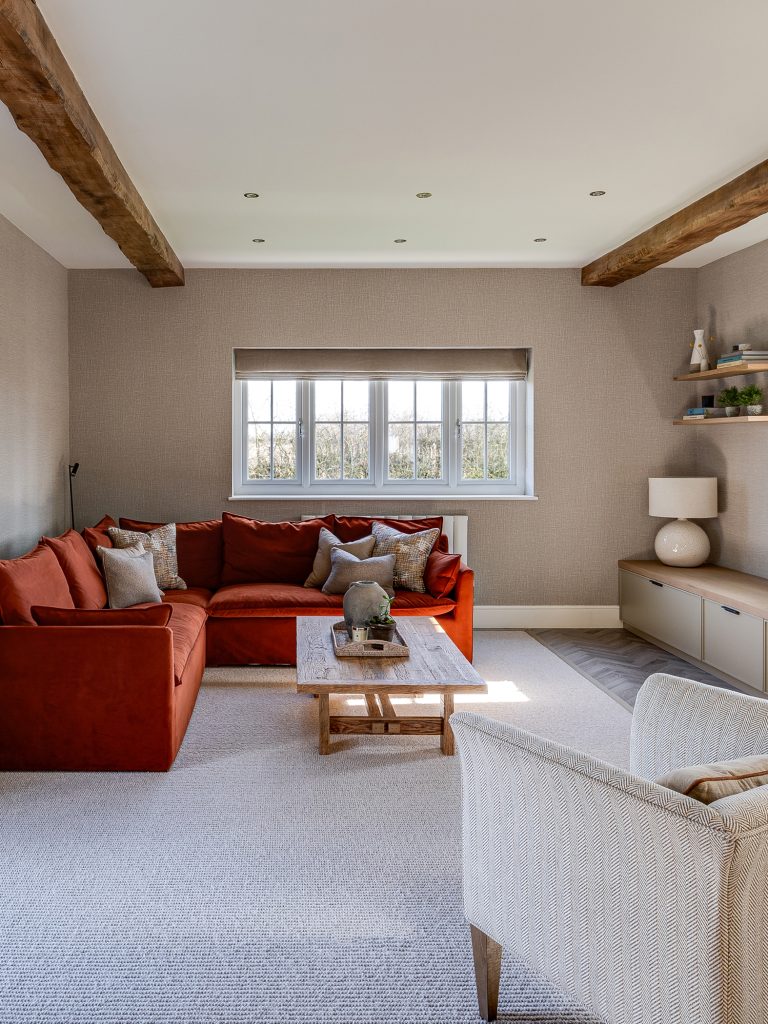 Cosy living room with rust-colored corner sofa, neutral armchair, wooden coffee table, and built-in shelving.