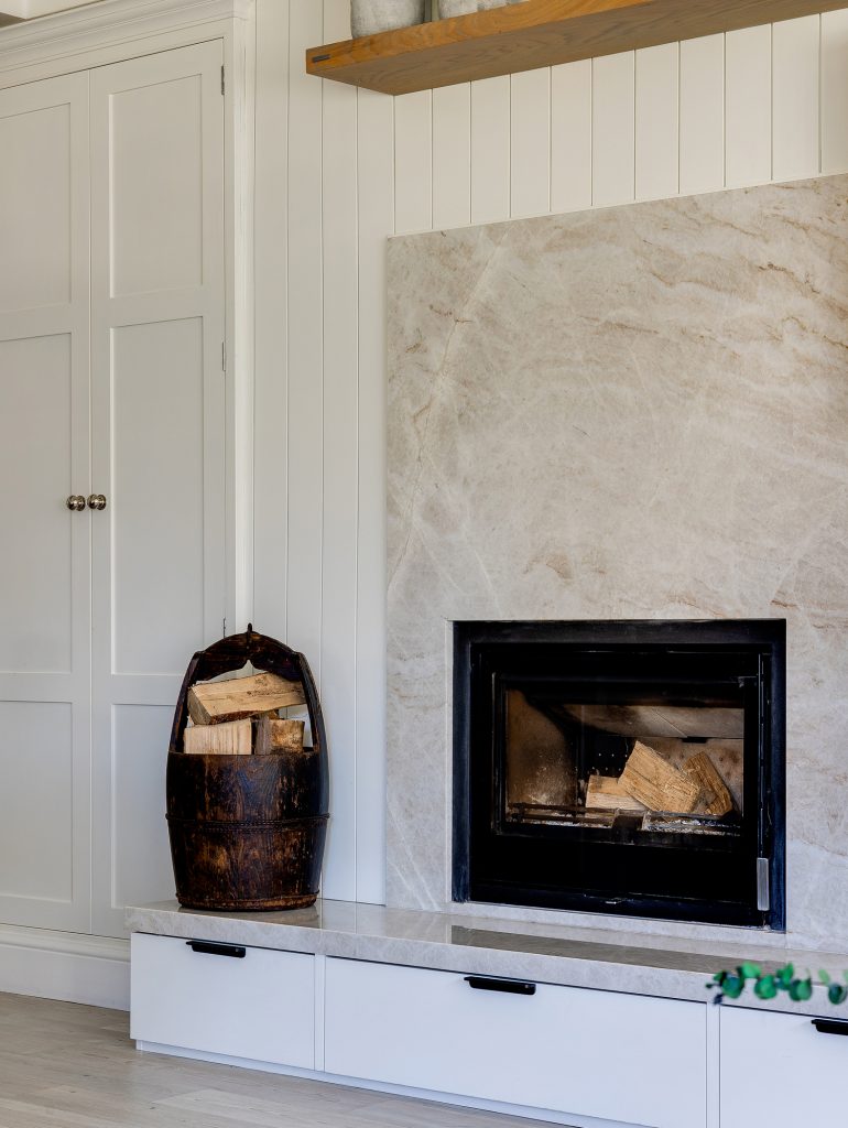Modern fireplace with a stone surround and a basket of firewood beside it.