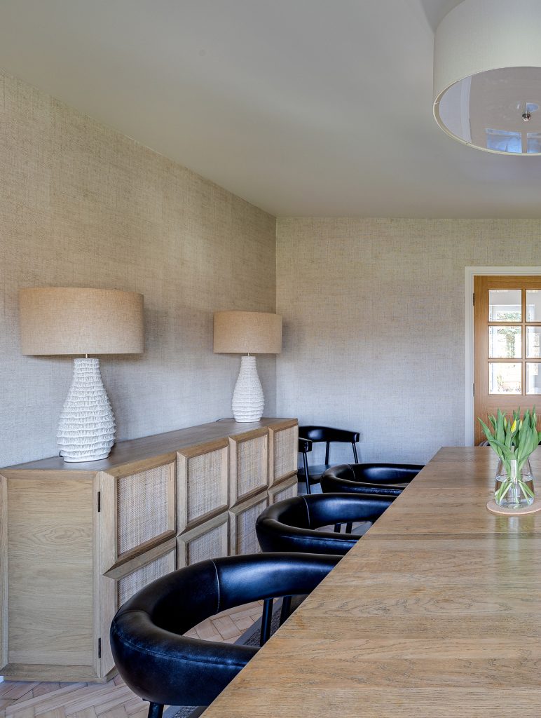Dining room with wooden table, black chairs, sideboard, and matching lamps in a neutral-toned interior.