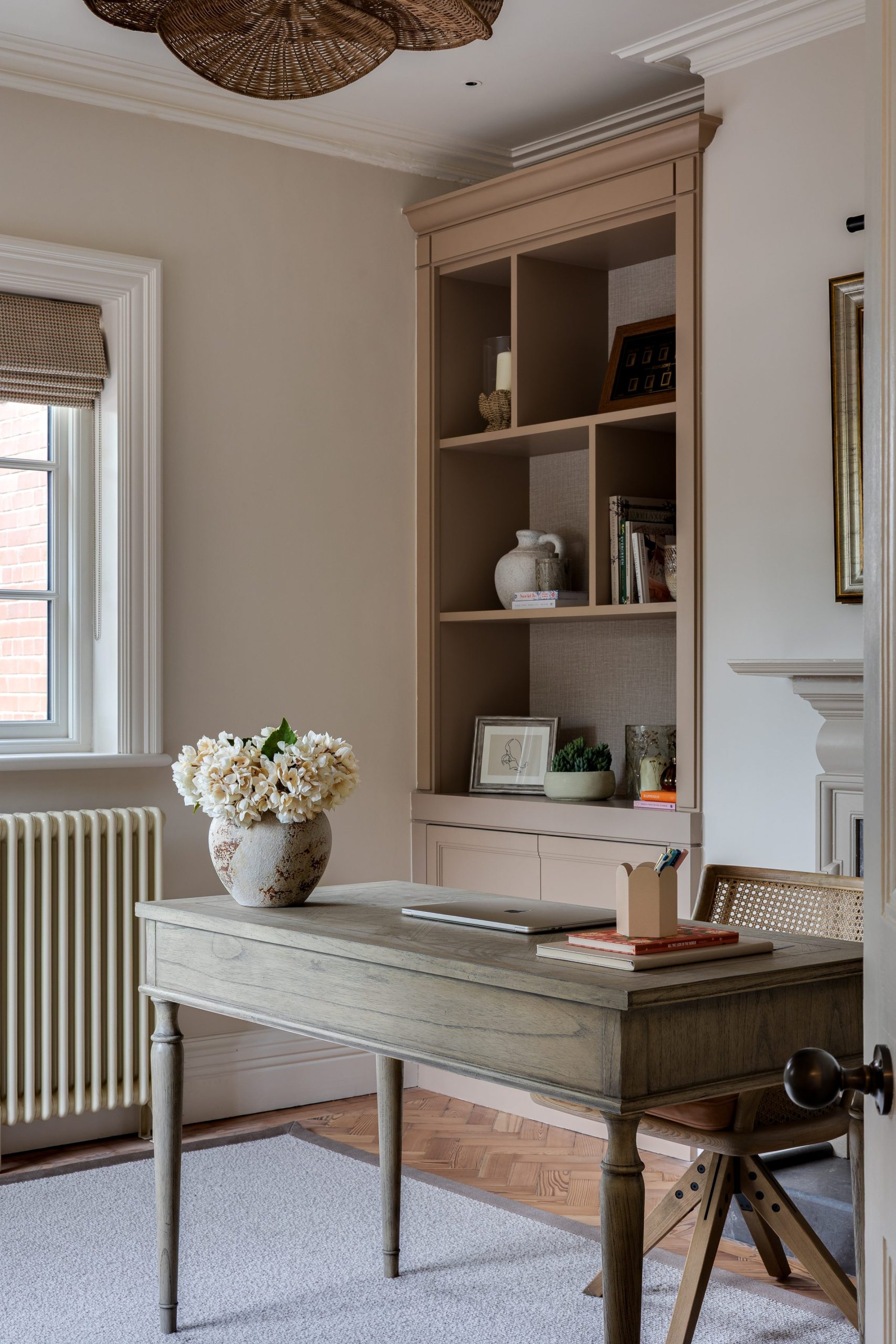 A home study with a wooden desk, laptop, and hydrangea arrangement, set against built-in shelving styled with ceramics, books, and framed art.