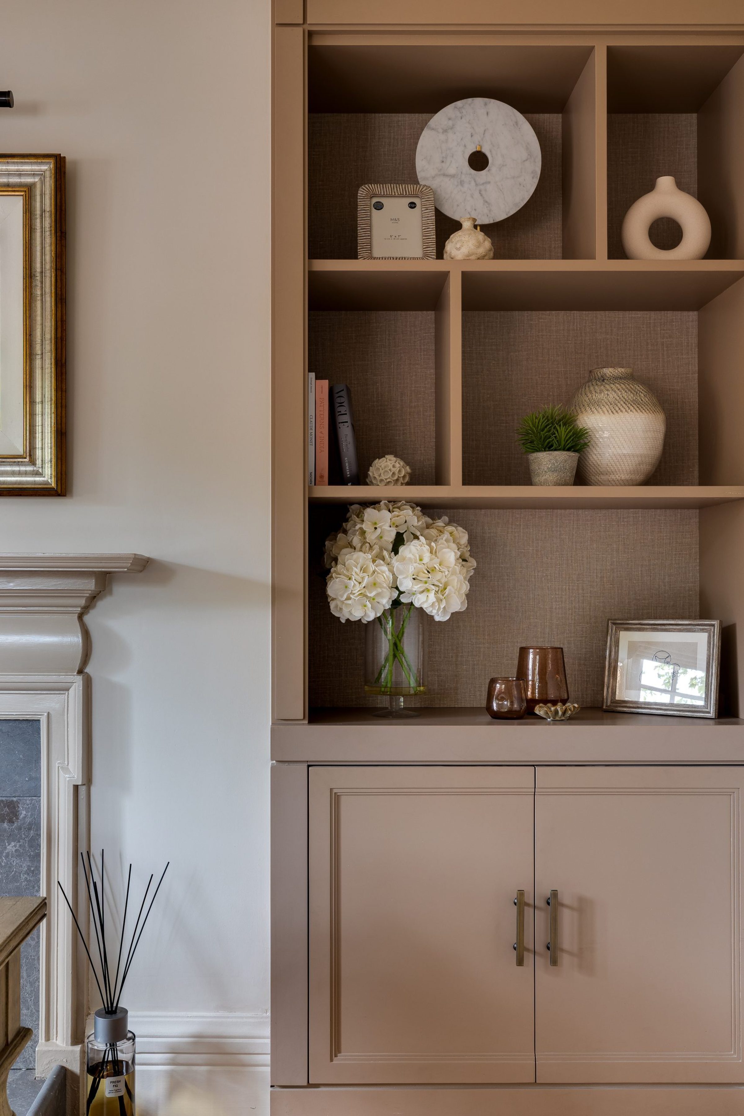 Built-in shelving in a study room, styled with books, ceramics, framed art, and a glass vase of white hydrangeas.
