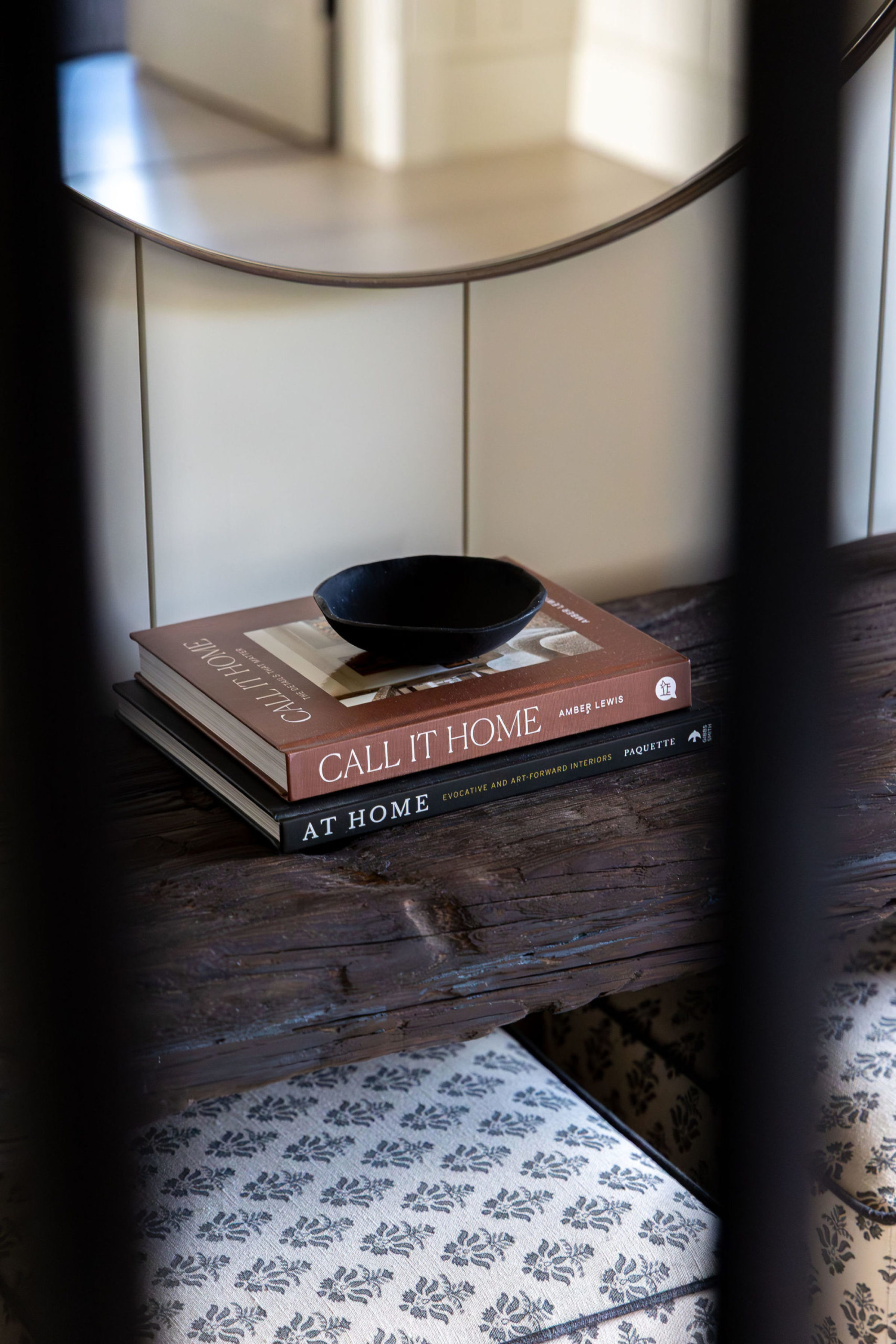 Close-up of stacked interior design books and a small black bowl on a rustic wooden console table.