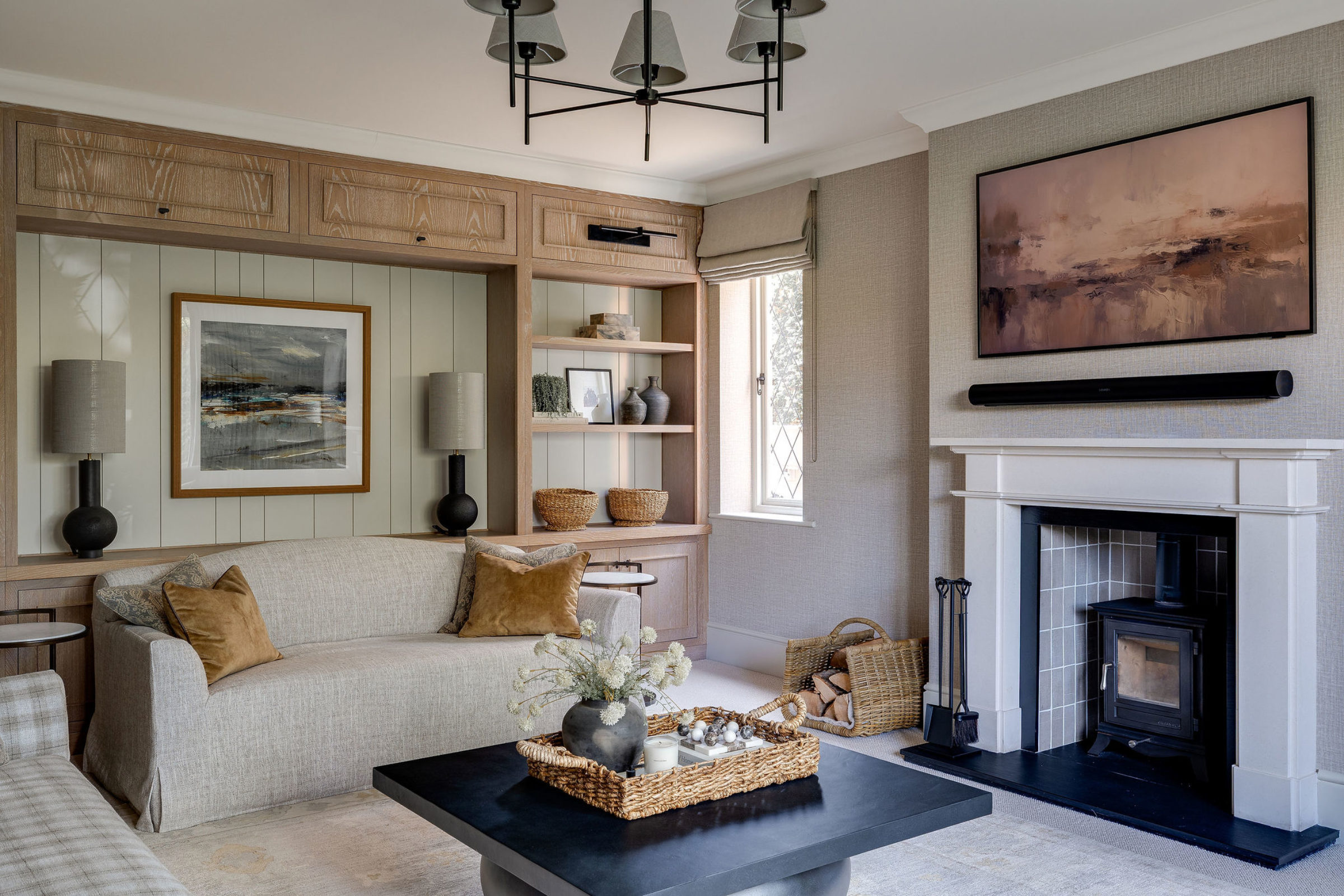 Elegant living room featuring built-in shelving, neutral sofa, modern fireplace with artwork above, and a black coffee table with a woven tray centerpiece.