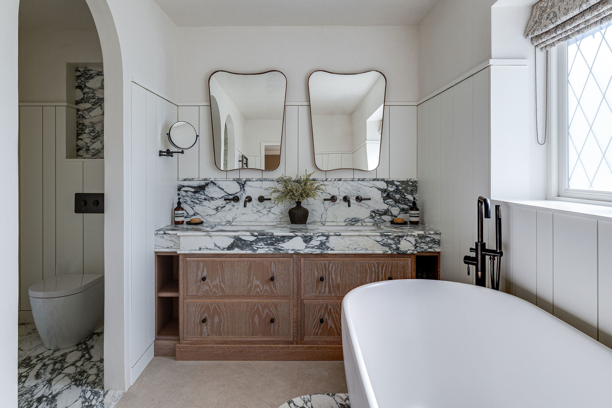 Modern bathroom with double vanity, marble backsplash, twin mirrors, and freestanding bathtub.