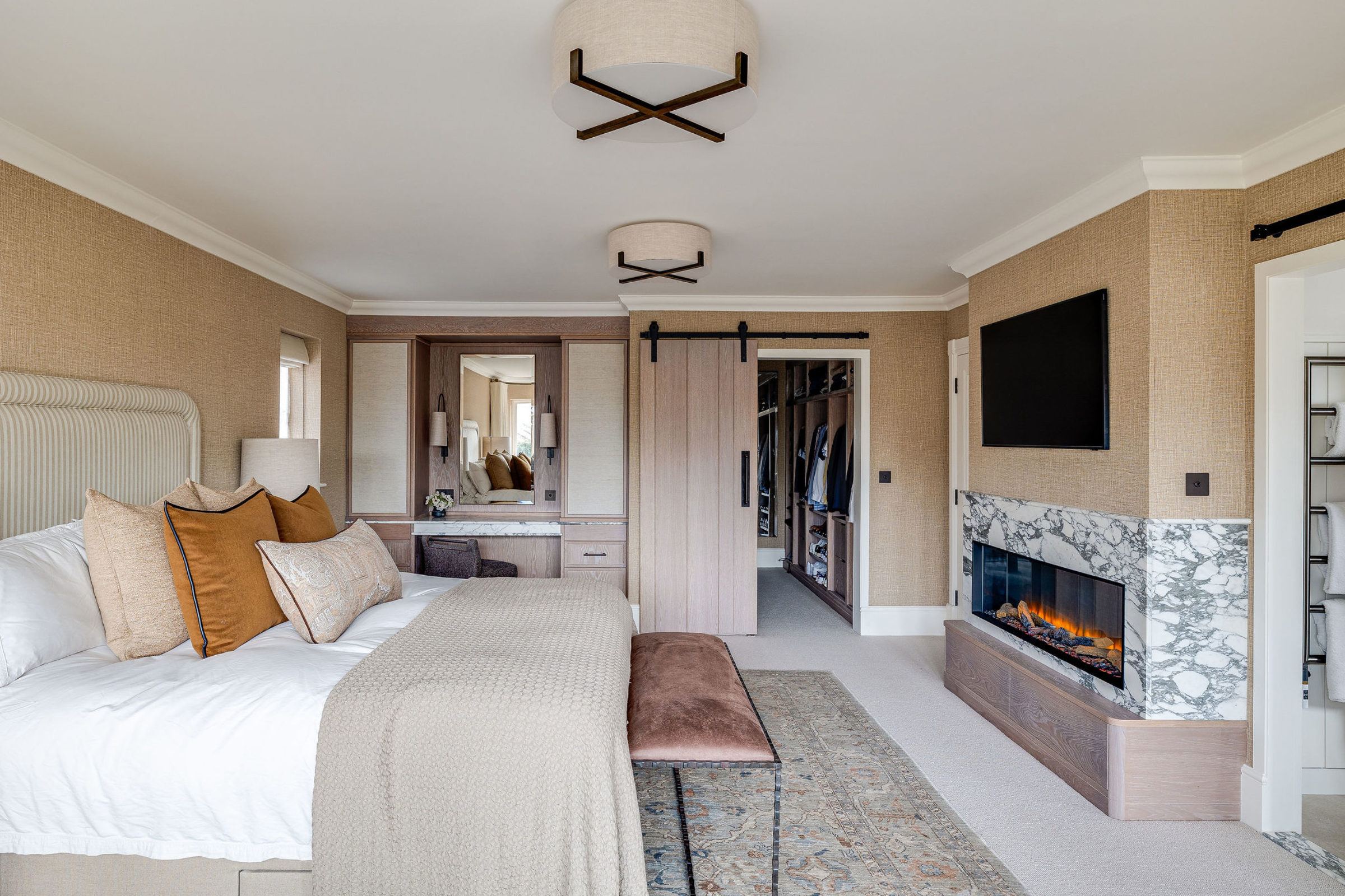 Elegant primary bedroom with marble fireplace, neutral bedding, and sliding barn door to walk-in closet.
