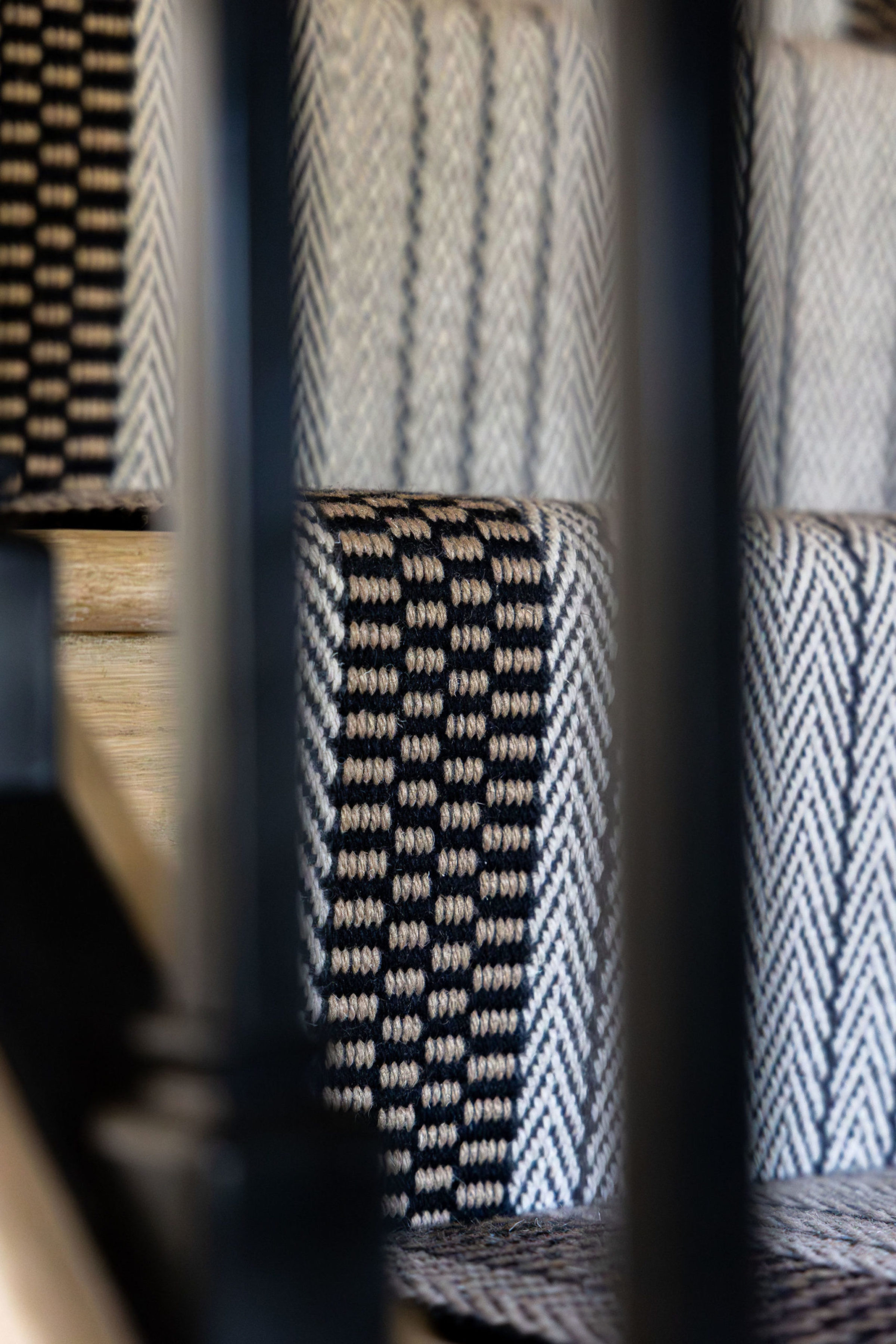 Detailed view of a textured herringbone and check-patterned stair runner between black stair rails.