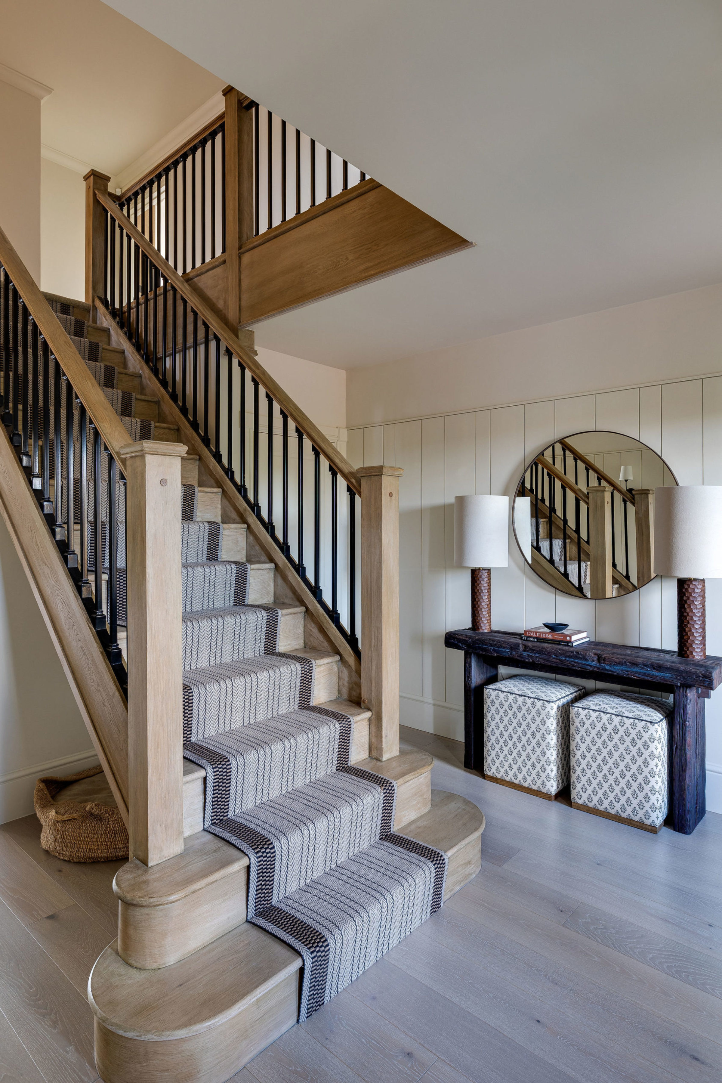 Entryway with wooden staircase, patterned runner, round mirror, and rustic console table.