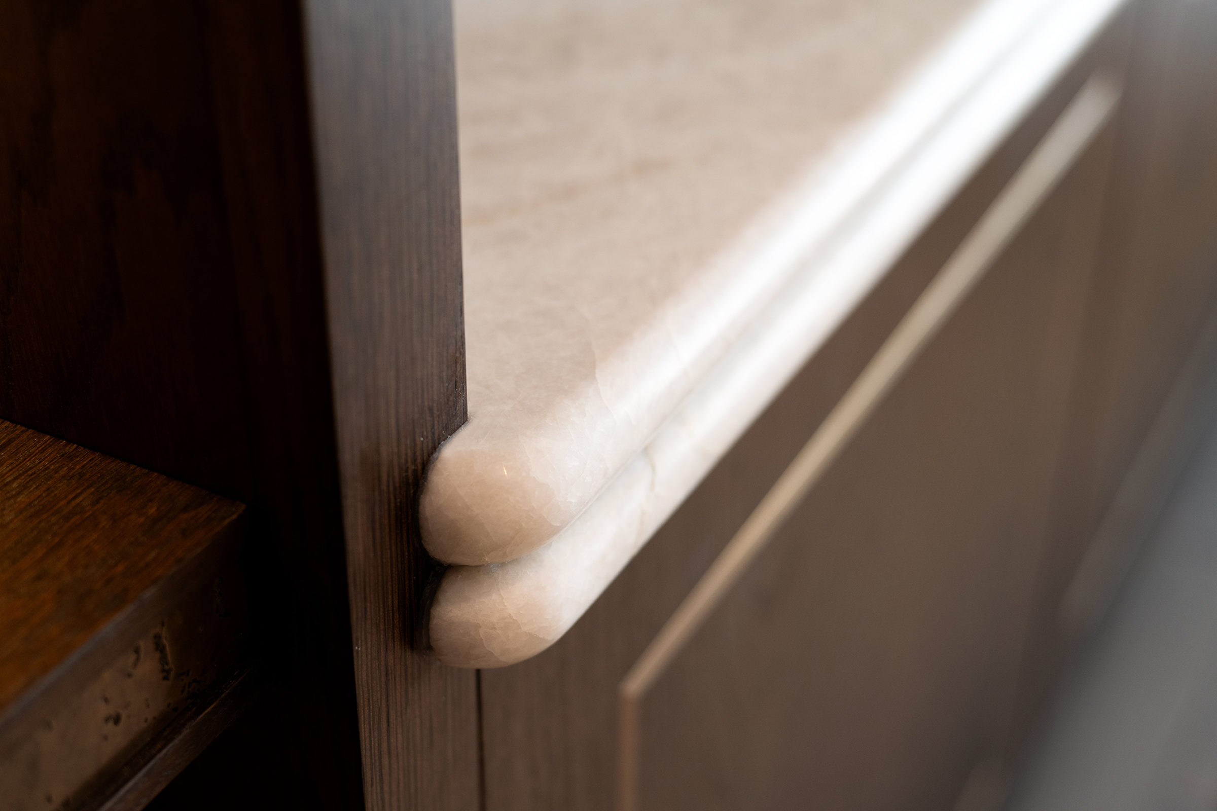 Close-up of a rounded pale marble countertop or windowsill edge with a smooth polished surface fitted against a dark wood vertical panel.